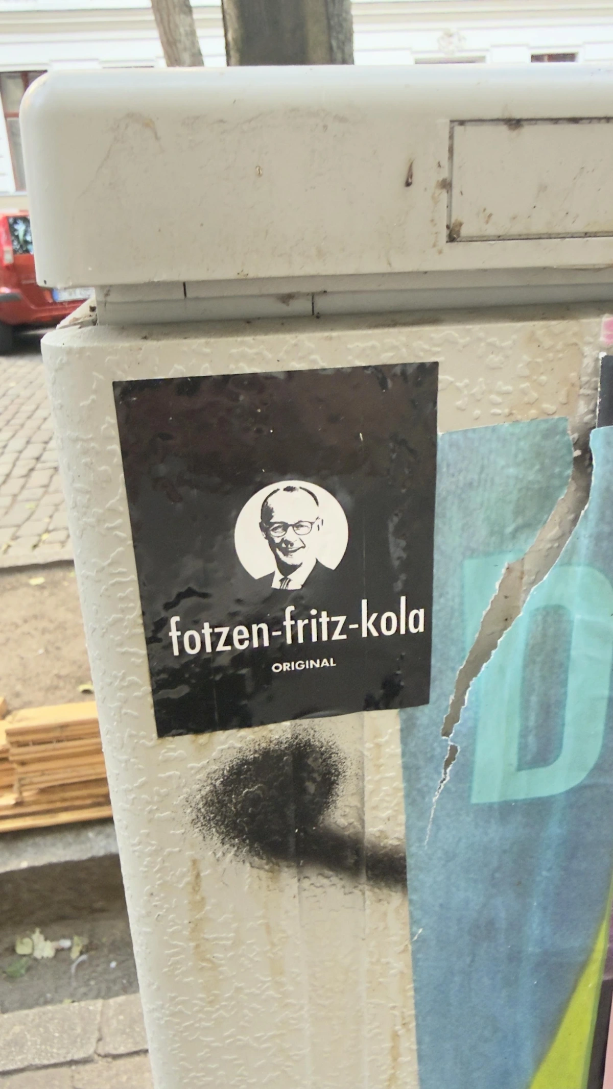 Ein Aufkleder mit dem Bild von Kanzler Merz. Darunter seht fotzen-fritz-kola original