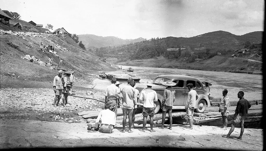 A group of men stand around a car disembarking from a river boat