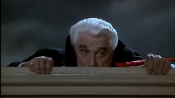 Leslie Nielsen in Dracula movie outfit peering from top of fence movie still image