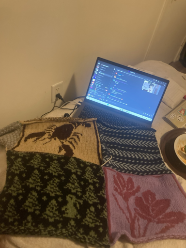 Four knitted squares sewn together. One is a design of a lobster, one is a chevron design, one is an image of a flower, and one is a design showing a rabbit lost in the woods