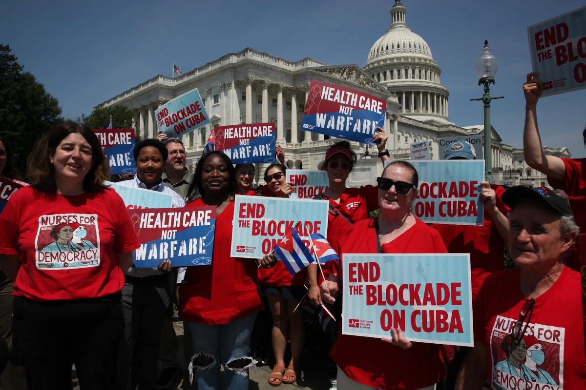 Photo of nurses in front of Capital Building in Washington, DC

Some are wearing red t-shirts saying "Nurses for Democracy". Some are holding signs with slogans: "End Blockade on Cuba" or "Healthcare Not Warfare", both with the logo of National Nurses United. 