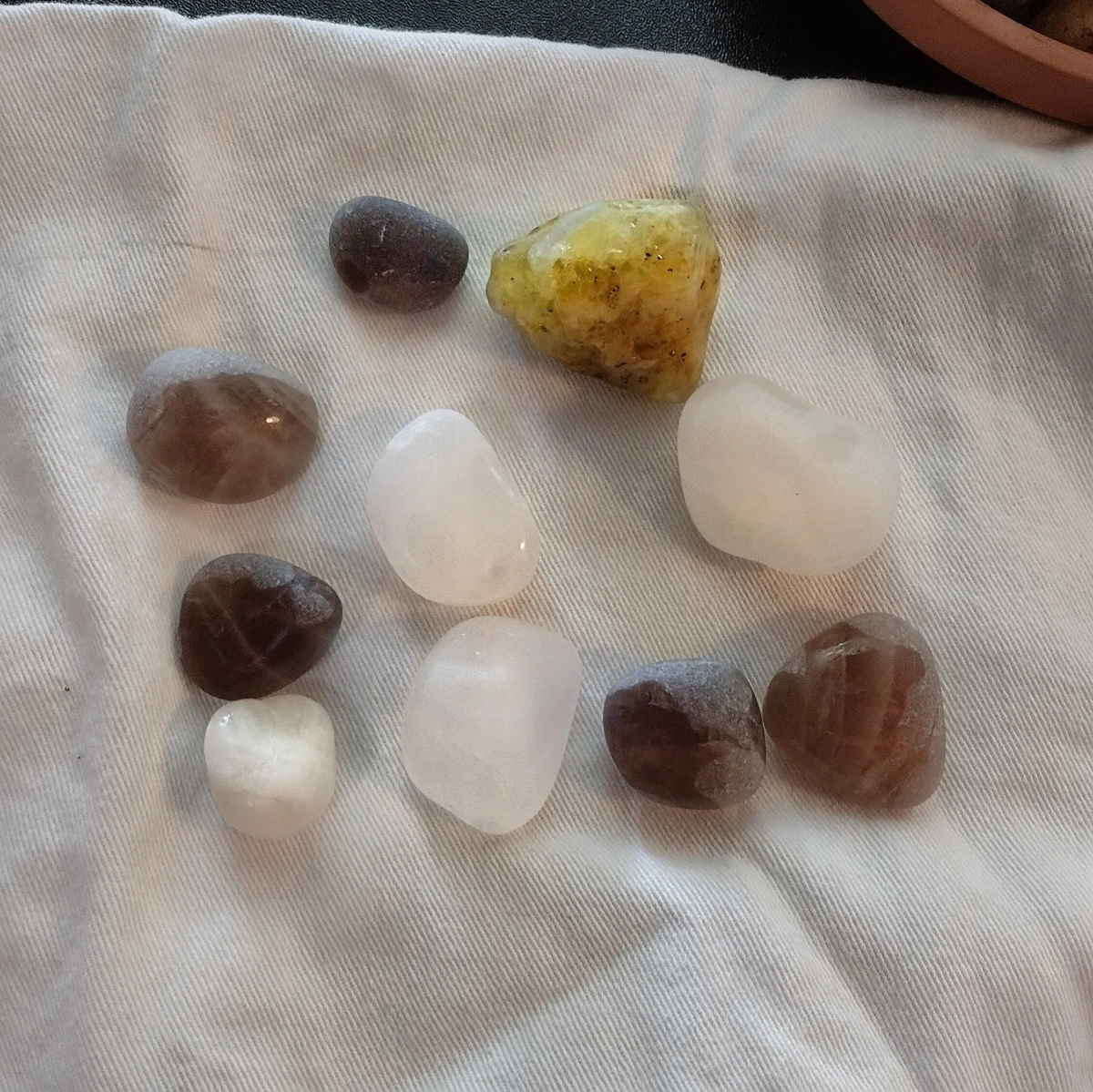 A collection of roughly tumbled rocks on a white napkin. Four are white quartz, five are smokey quarts, one is rougher and green of unknown type.
