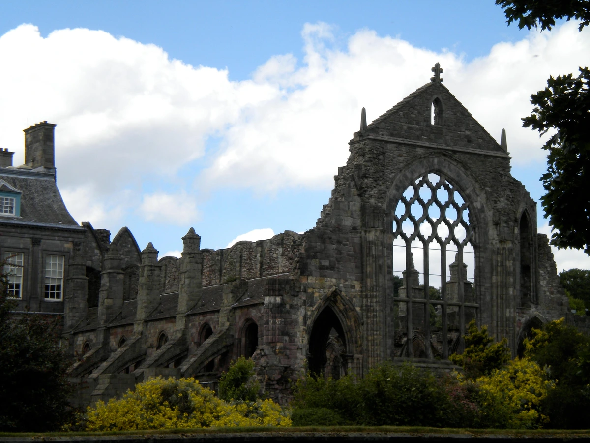 "the remains of holyrood: about half the original height of the side walls and the full height of one end wall with large, empty, window. the sky is blue with white clouds."