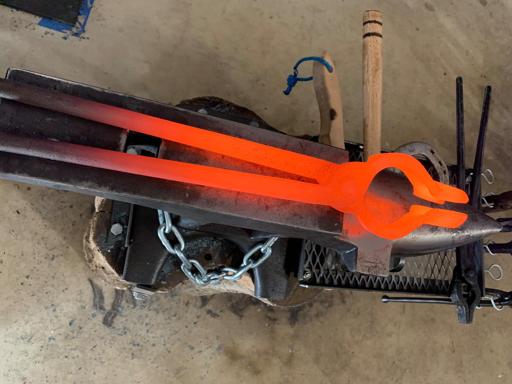A glowing red hot pair of tongs sits atop a small anvil, which was my first anvil.