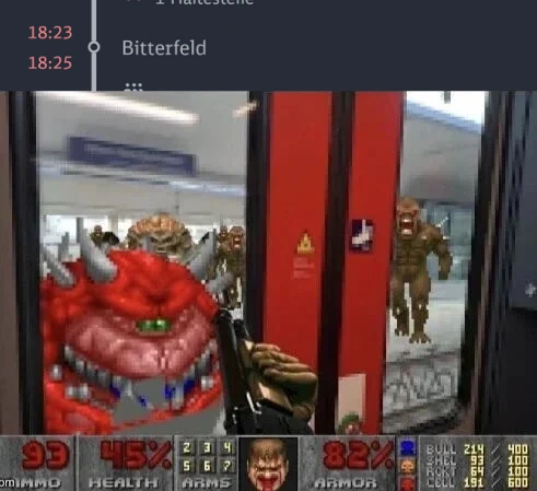 Ein Meme, das die Benutzeroberfläche des Ego-Shooter-Spiels "Doom" (1993) über ein Foto legt, das aus dem Inneren eines Zuges aufgenommen wurde. Der untere Teil des Bildes zeigt den klassischen "Doom"-HUD mit Gesundheitszustand (93 %), Rüstung (45 %) und dem Gesicht des Spielcharakters. Der Blick durch die Zugtüren zeigt einen Bahnsteig, auf dem statt Menschen mehrere Dämonen aus dem Spiel stehen, darunter Imps und ein Cacodemon. Oben im Bild ist eine digitale Haltestellenanzeige eines öffentlichen Verkehrsmittels zu sehen, die den nächsten Halt anzeigt: "18:25 Bitterfeld".