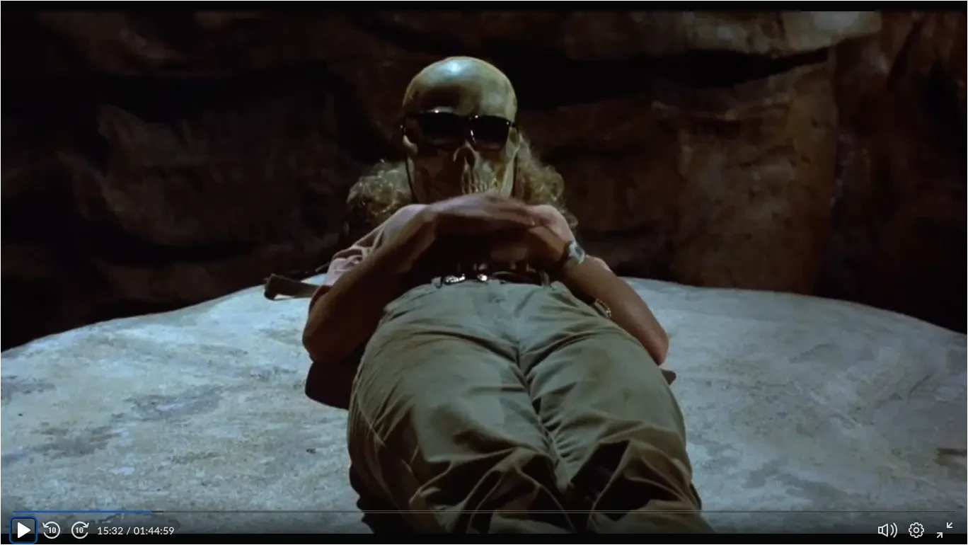 Firewalker - Patricia lying on a sarcophagus, with a skull wearing sunglasses covering her face