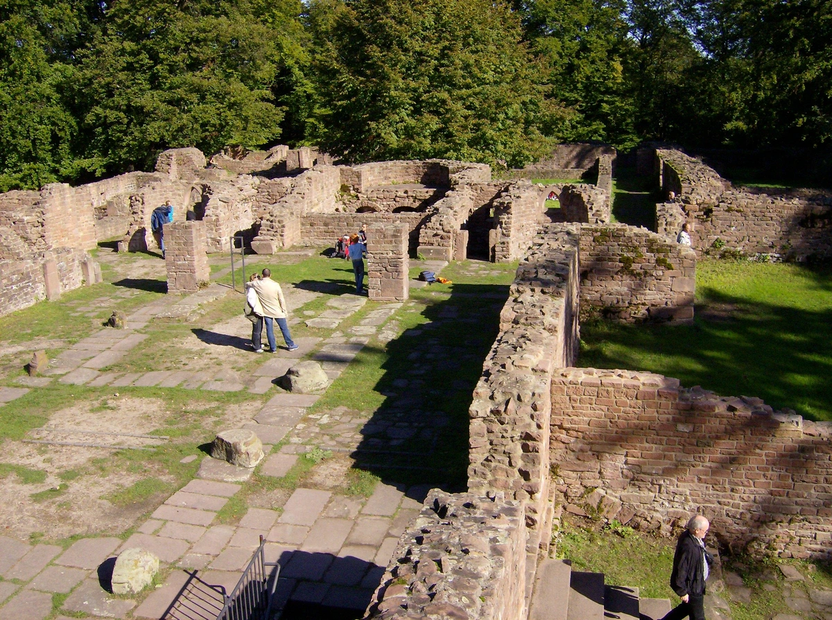 overhead view of the ruins of thick stone walls surrounding an open area to the left. the walls are about 2 meters tall and 2/3 meter wide, and there are about 6 tourists at various places among the ruins.