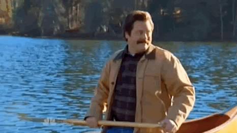 Ron Swanson from Parks & Recreation, happily paddling a canoe on a beautiful lake.