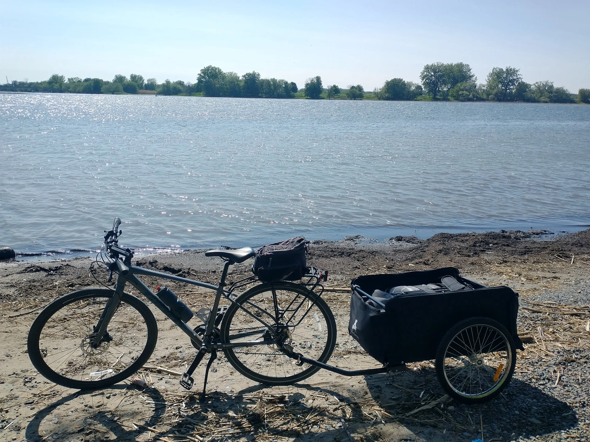 A bicycle on the shore with a trailer carrying an inflatable kayak
