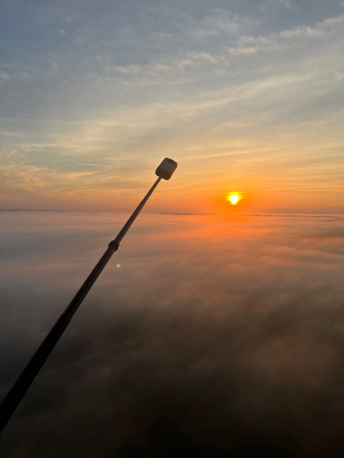 Sunrise from in the air with fog below. Insta360 camera on a selfie stick is sticking out into the frame.