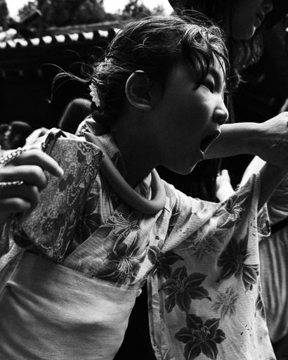 Japanese child wearing traditional suit being dragged by the hand by her mother. The photograph is taken from a close point of view. Her mouth is with open like she is screaming.