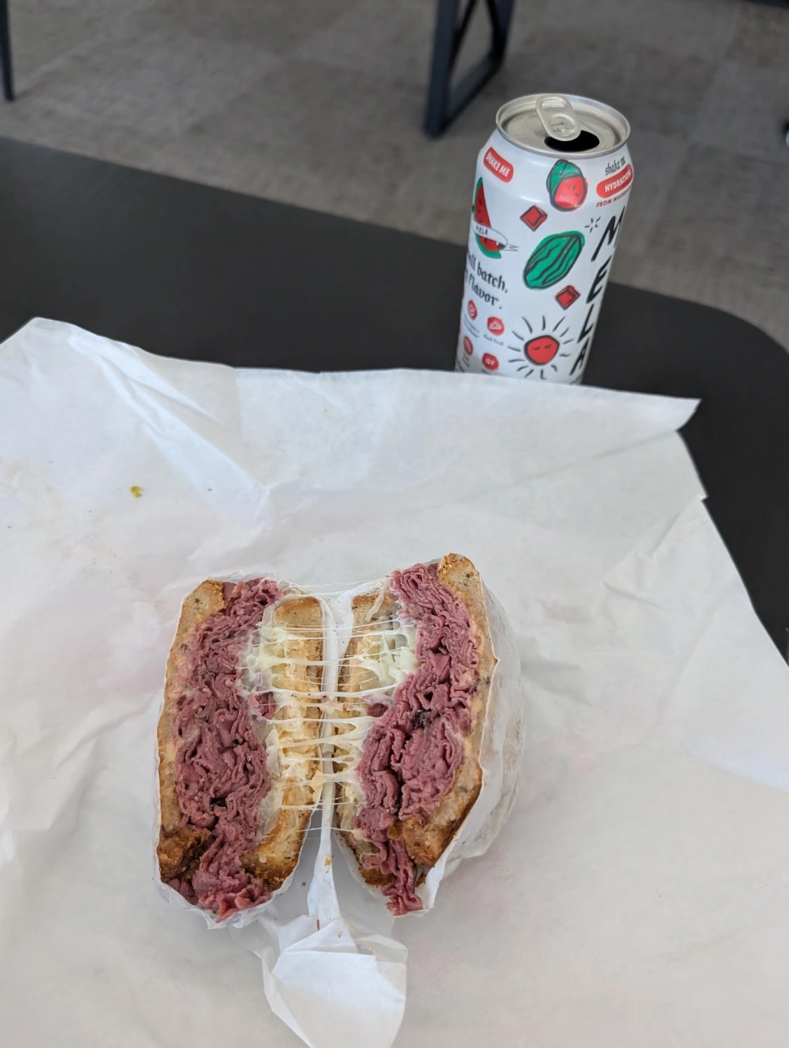 A pastrami sandwich sliced in half, with gooey strands of swiss cheese connecting the two sides.