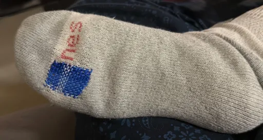 A photo of the bottom of a white sock. A hole has been repaired with a woven blue patch that has several shades of blue in it 