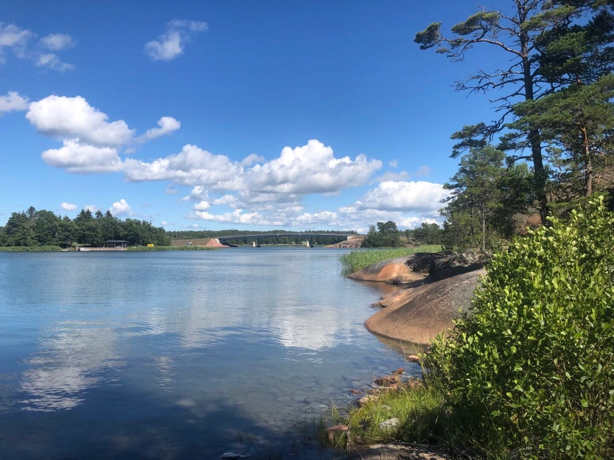 Photo from a cliff over calm waters towards a bridge and a blue sky with a few clouds.