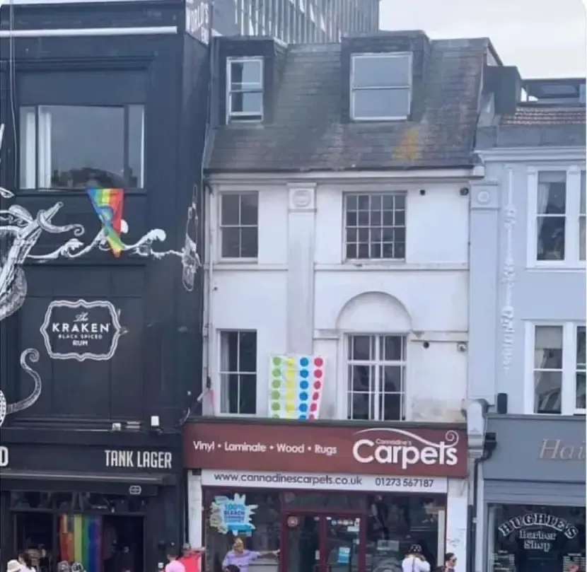 A picture of small shop with some houses above it. There's a Twister board hung up outside, like a flag.