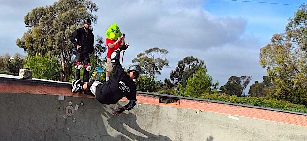 A photo of a skateboarder grinding the coping with The Grinch on deck watching