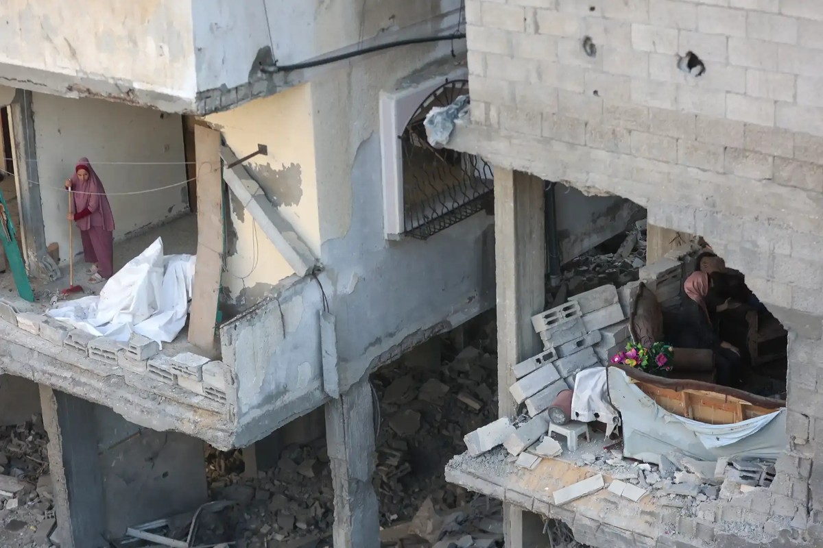 A Palestinian woman sweeps debris from her home as her neighbour inspects the damage.