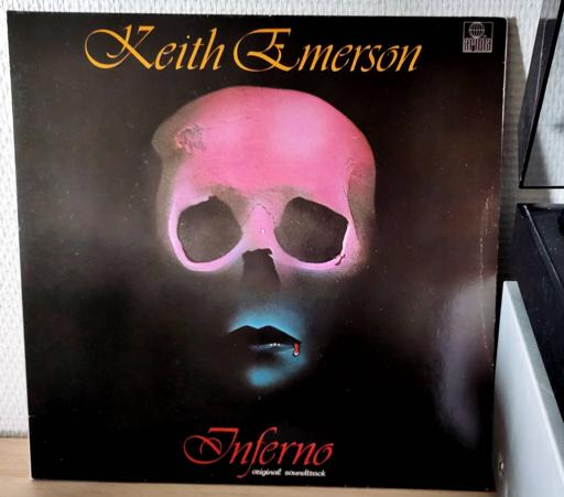 The cover art is of a pink and blue skull with a lipstick mouth that has a trickle of blood running from one corner. All on a black background, artist's name in gold orange on top, title in red at bottom.