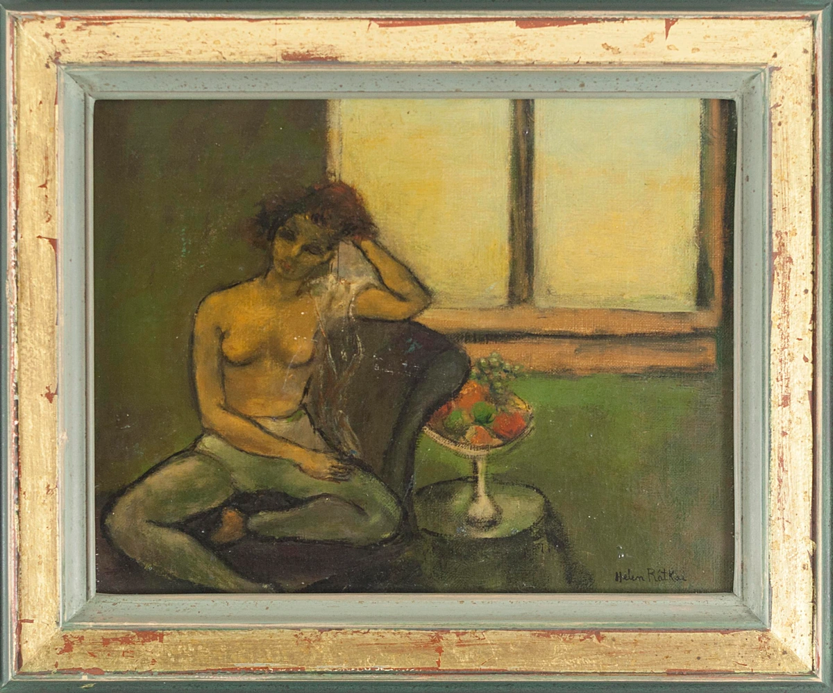 A seated nude woman with reddish-brown hair rests her right hand against her head in a contemplative pose, her body turned slightly toward the viewer. A dark drape falls across her lap. Beside her, a pedestal bowl holds colorful fruit — grapes, oranges, and apples. A window with warm yellow light fills the background. The palette is muted olive green and ochre. Signed lower right: Helen Ratkee. Oil on canvas, intimate in scale and mood.