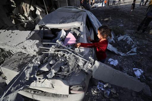 A Palestinian girl scribbles on a car crushed by falling concrete at the site of an Israeli strike on a house, in Jabalia.