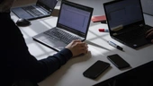 Vorschaubild zeigt Laptops auf Tisch, eine Person im Anschnitt