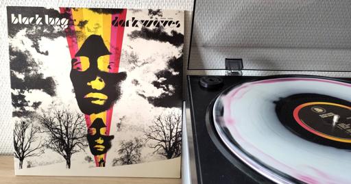 The album cover is a high contrast black and white landscape photograph with a low horizon line. down through the middle a magenta, orange and yellow "rainbow" overlaps the photograph, tapering downward. Within the coloured band, two identical female faces are mounted in negative. Next to the album cover, the gorgeous coloured disc spins on the turntable.