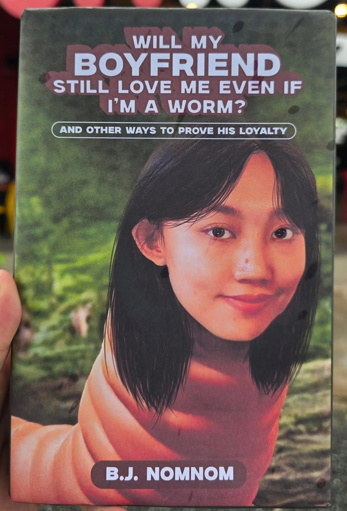 A book that seems to have the title "WILL MY BOYFRIEND STILL LOVE ME EVEN IF I'M A WORM?" with the subtitle being "And other ways to prove his loyalty". Cover art of a woman's head superimposed over a wom's body. Author "B.J. NOMNOM".