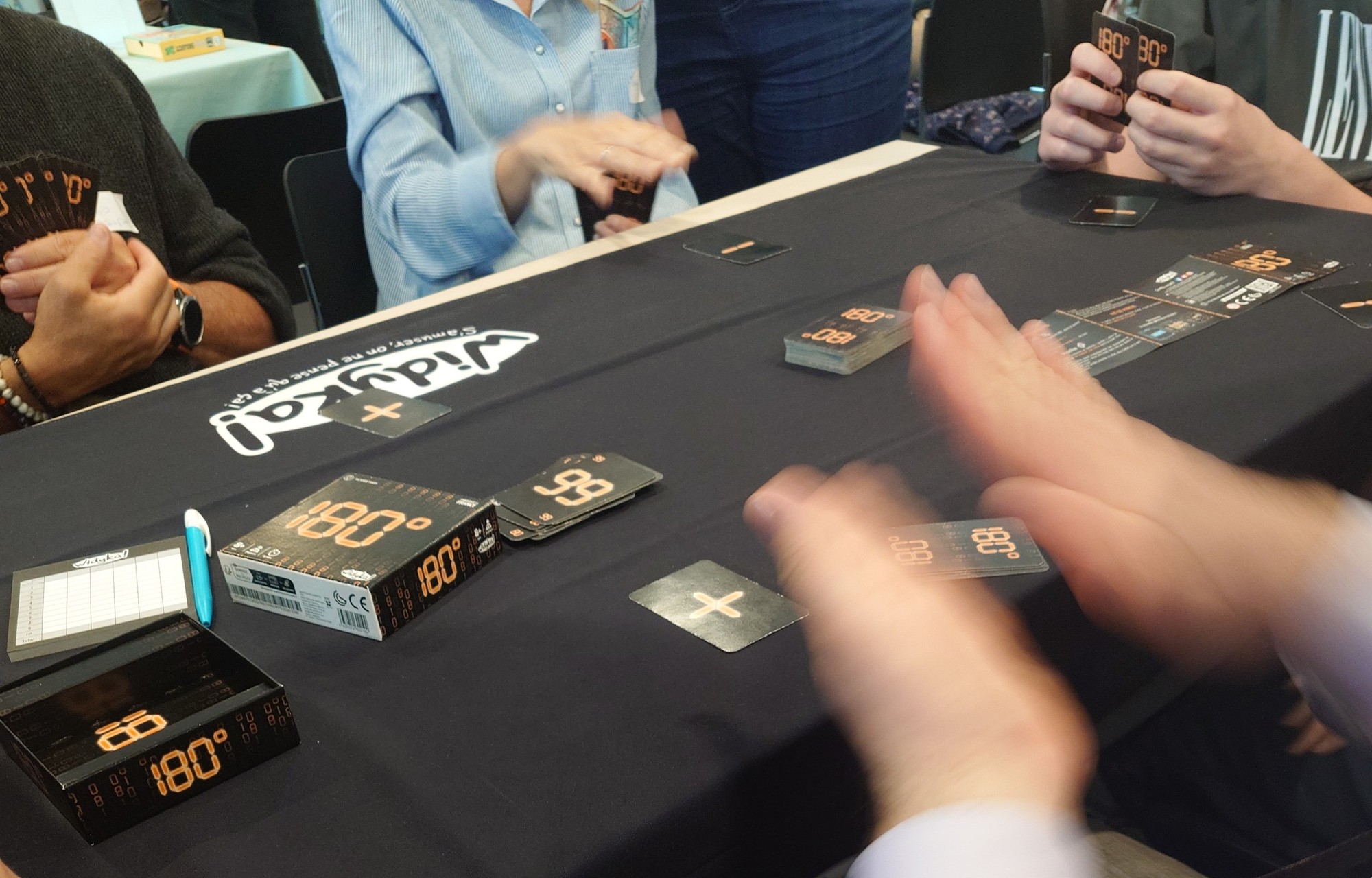 Photo du jeu 180°, les joueurs ont des cartes + et - posé devant eux et tiennent dans leur main des chiffres