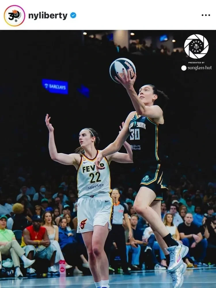 Breanna Stewart making a layup. Caitlin Clark is behind her, raising her arms in frustration, looking off to a ref outside the frame.