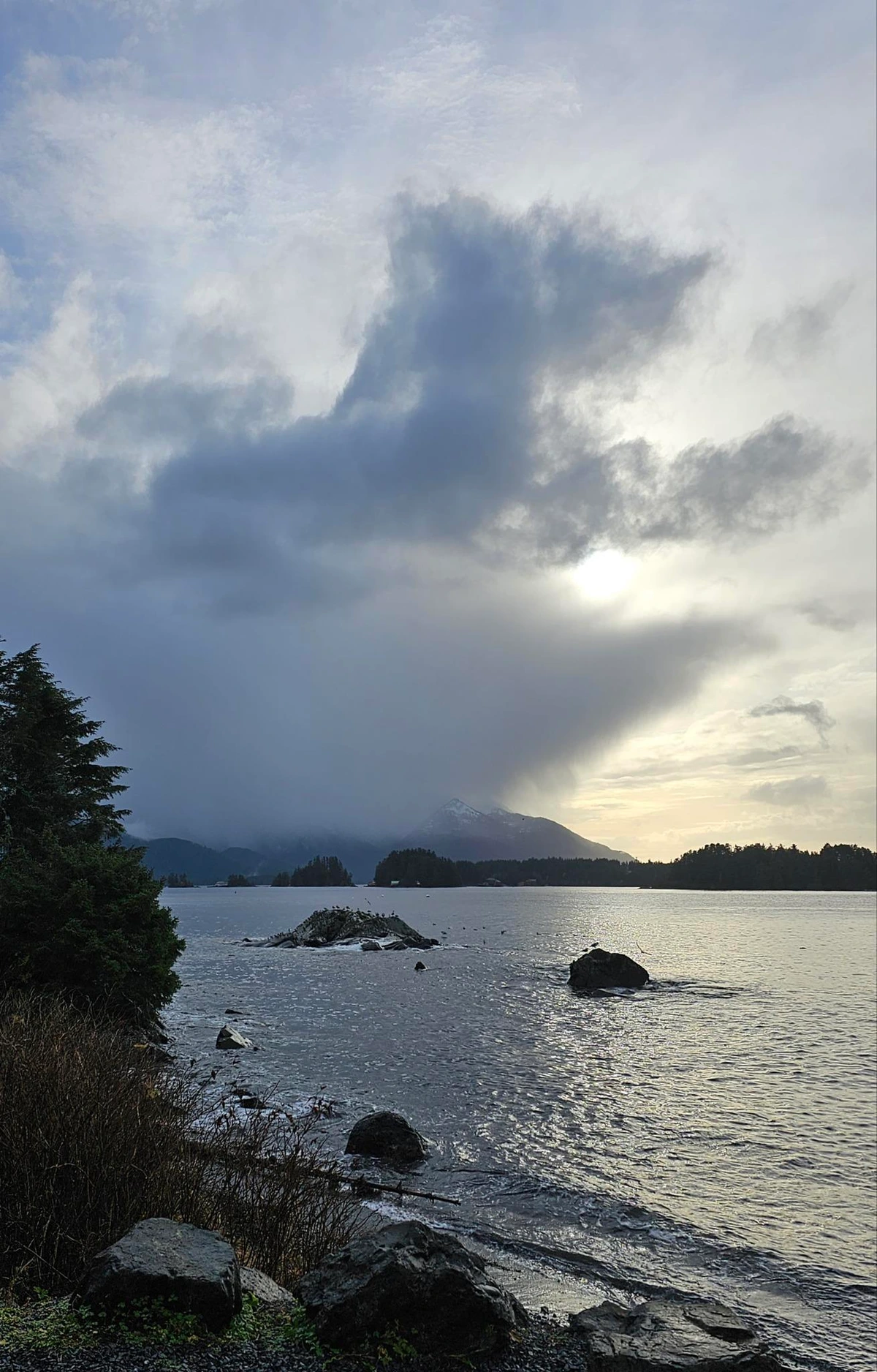 A pic overlooking the channel, waves lapping at the shore and the gray clouds in the distance are in the distinct shape of a mermaid. Her hair is blowing to the right, her back is slightly turned toward us with an arm coyly over her chest. Her tail is bent back - she appears to be sitting on it.